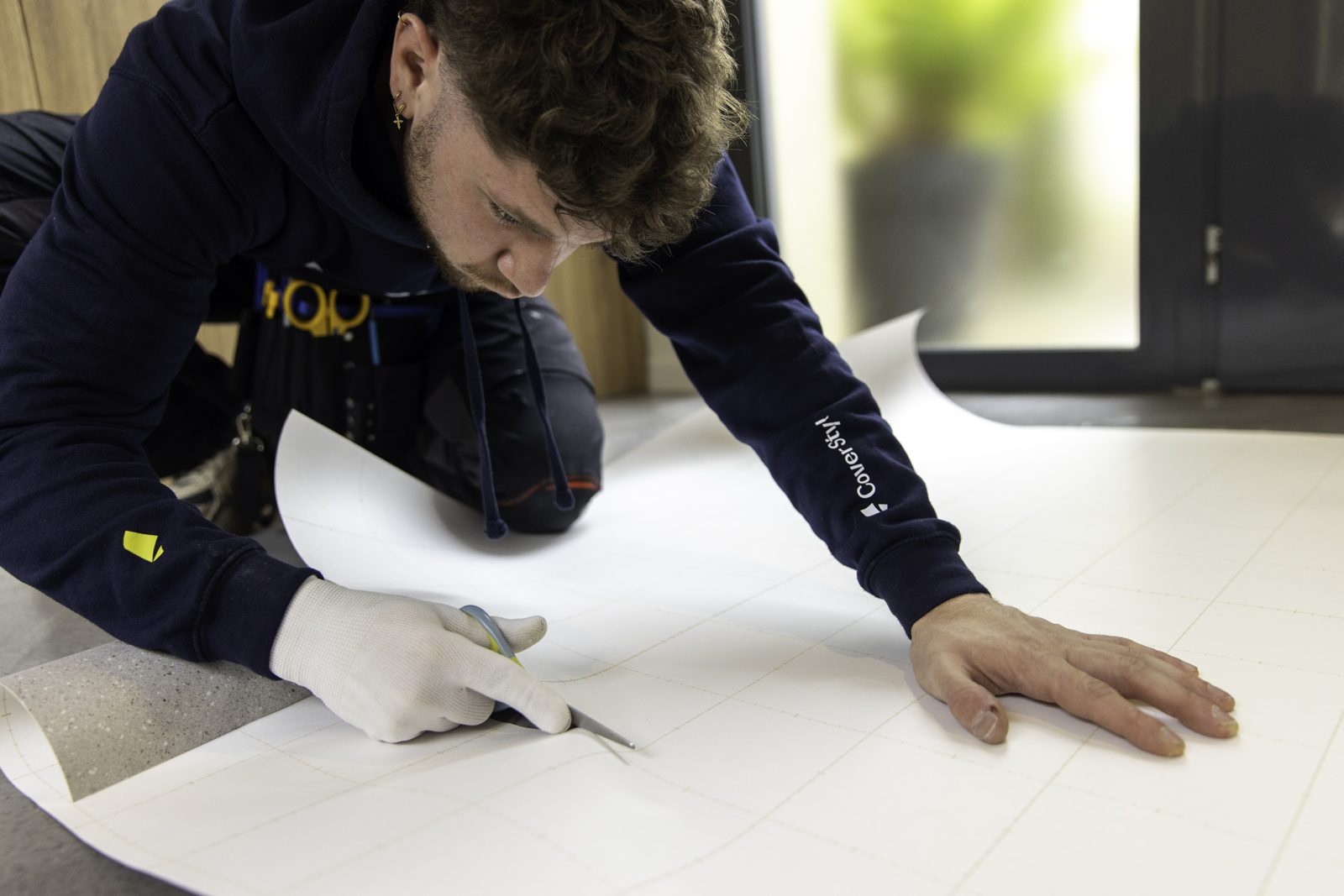 Instalador cortando una tira de lámina sobre el piso, siguiendo la cuadrícula del papel
